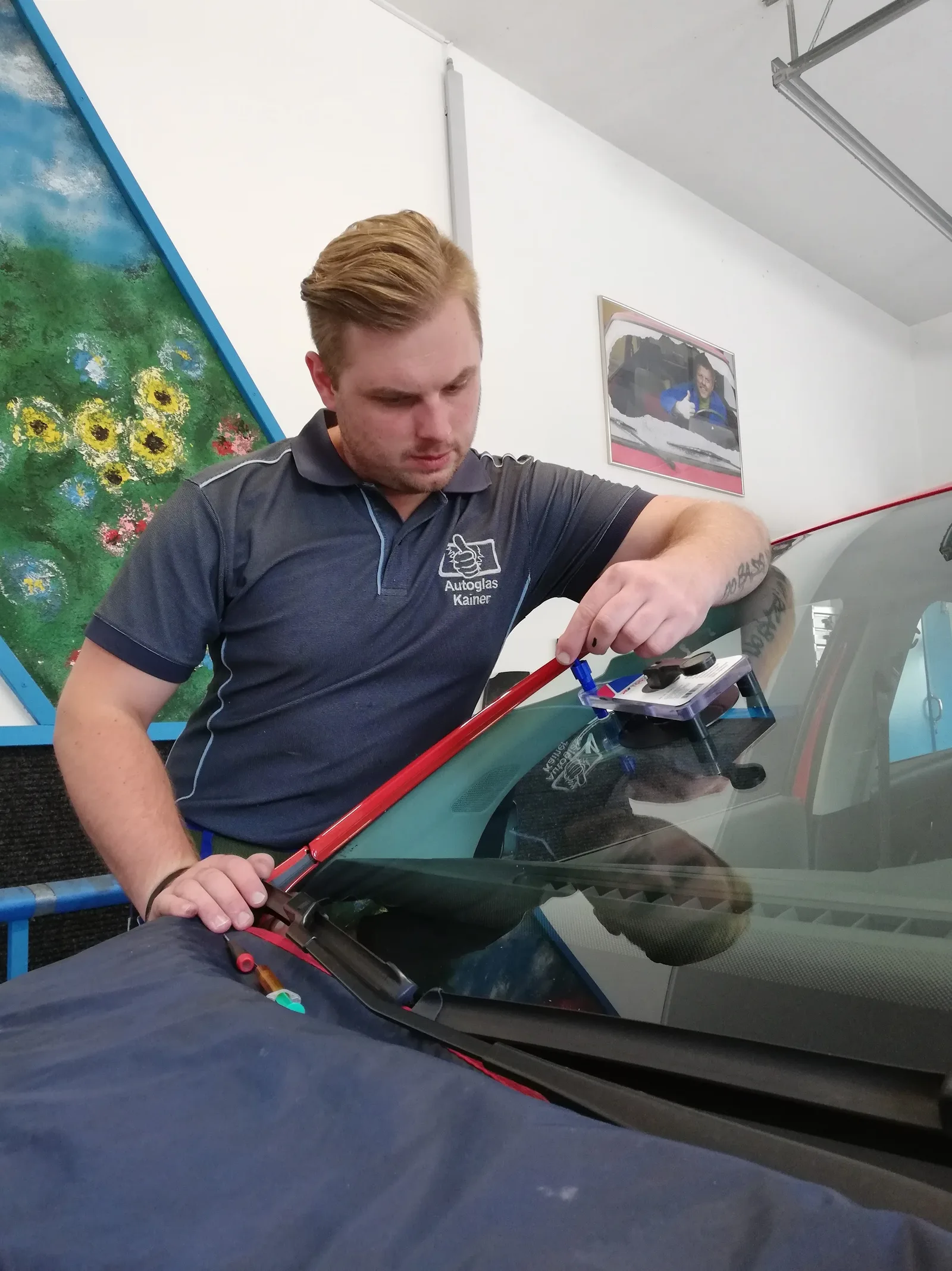 Mitarbeiter im Poloshirt mit Firmenzeichen löst eine Windschutzscheibe mit einem roten Schneidewerkzeug